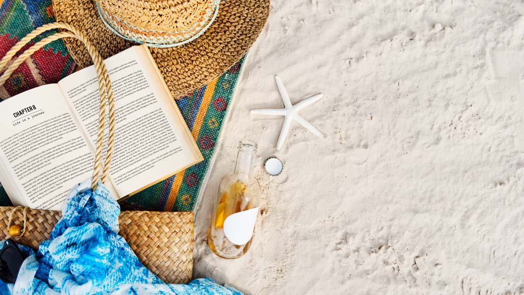 Απαραίτητα για την παραλία: Τσάντα θαλάσσης, βιβλίο, καπέλο, beachwear, γυαλιά ηλίου, πετσέτα θαλάσσης πάνω σε άμμο