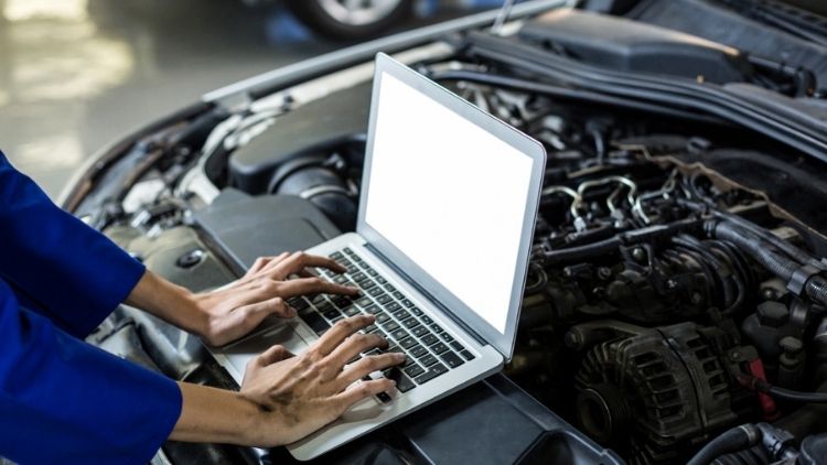 Χέρια μηχανικού δουλεύουν σε laptop με ανοιχτό καπό αυτοκινήτου.