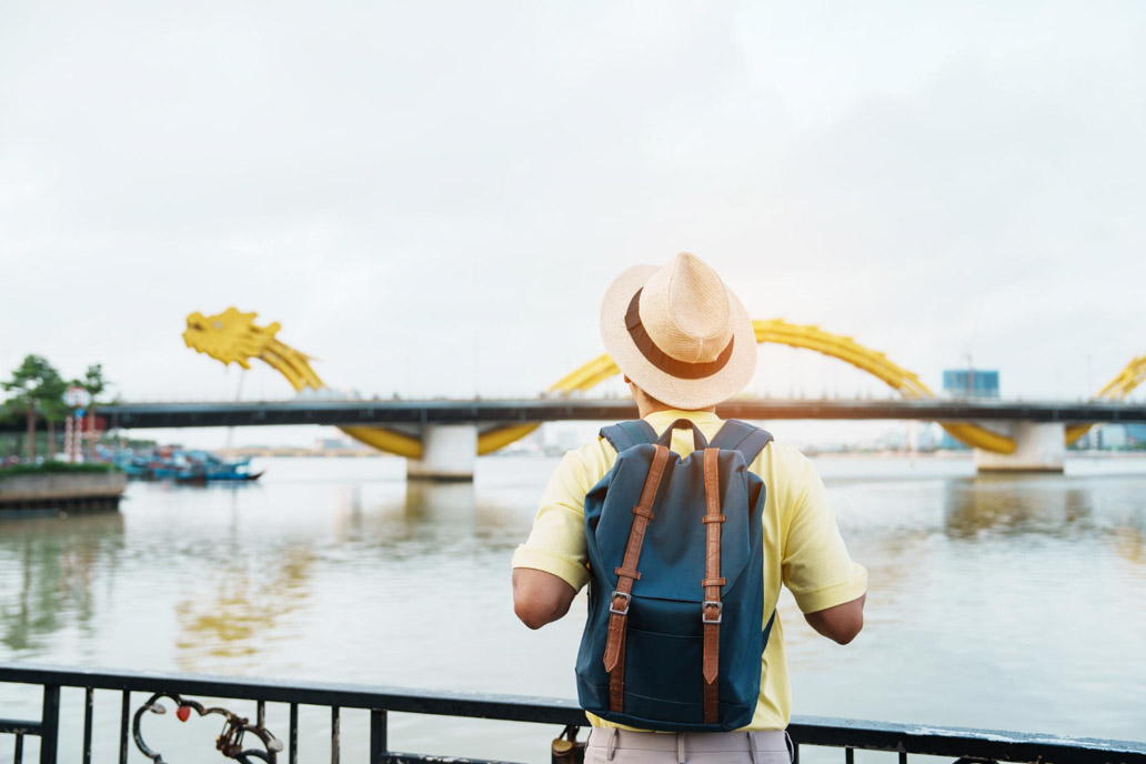 Μοναχικός ταξιδιώτης με καπέλο κουβαλάει τσάντα και στέκεται μπροστά από ένα ποτάμι.