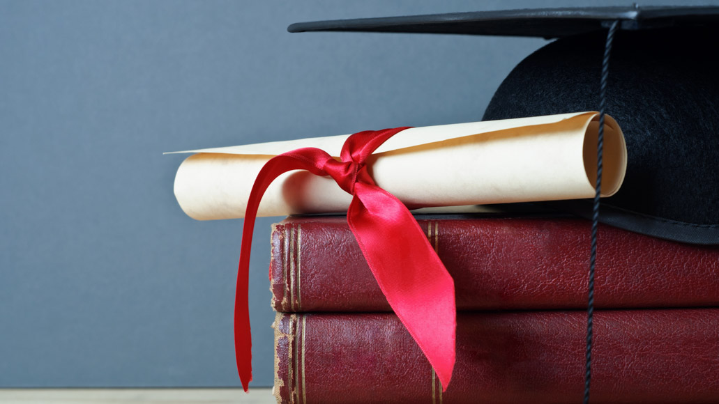 Θεματική εικόνα για το γιατί να κάνω διδακτορικό. Πτυχίο με κορδέλα στέκεται πάνω σε 3 βιβλία και δίπλα σε καπέλο αποφοίτησης.