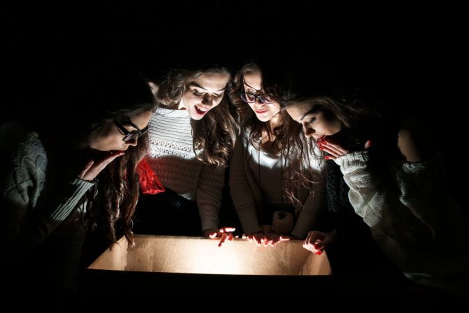 Εφηβικό πάρτυ σε δωμάτιο απόδρασης (escape room). Τέσσερις έφηβες κοπέλες κοιτούν μέσα σε φωτισμένη κούτα.