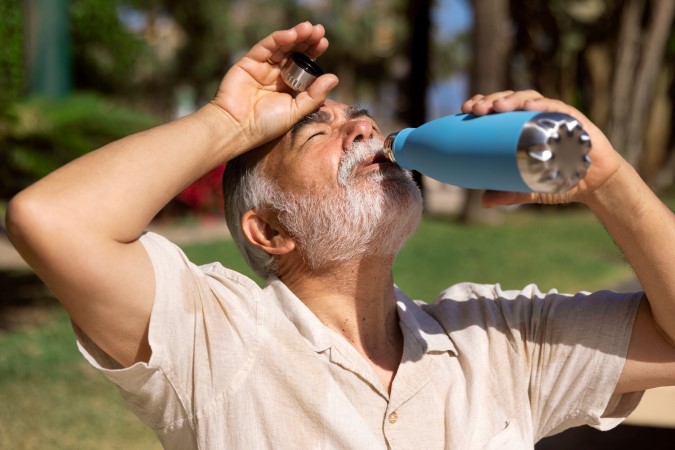Ηλικιωμένος πίνει νερό από μπλε παγούρι για να αποφύγει τη θερμοπληξία.