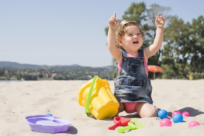 Χαρούμενο μωρό κορίτσι παίζει με παιχνίδια παραλίας στην άμμο. 