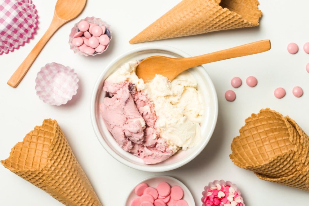 Σπιτικό παγωτό με γεύση βανίλια και φράουλα σε μπολ και γύρω γύρω κώνοι παγωτού και σοκολατάκια.