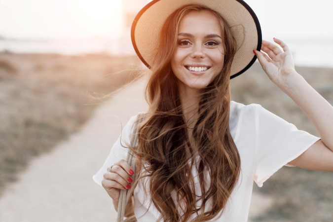 Χαμογελαστή γυναίκα με καλοκαιρινό καπέλο και ντύσιμο στην εξοχή. 