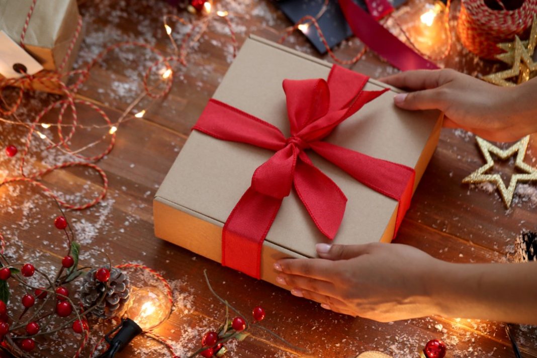 Θεματική εικόνα για πρωτότυπα χριστουγεννιάτικα δώρα. Άτομο ετοιμάζεται να ανοίξει ένα κουτί τυλιγμένο με κόκκινη κορδέλα.