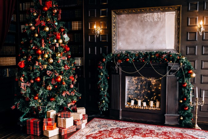 Χριστουγεννιάτικο δέντρο με δώρα μπροστά του και χριστουγεννιάτικα στολισμένο τζάκι μέσα σε σαλόνι.