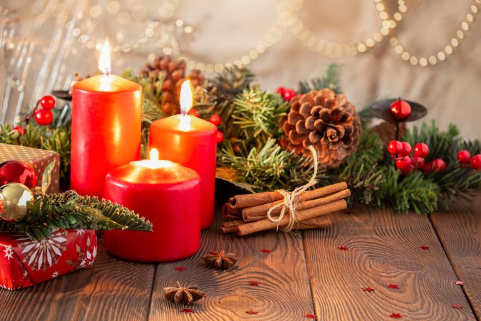Όμορφο χριστουγεννιάτικο δώρο. Τρία κόκκινα αρωματικά κεριά δίπλα σε χριστουγεννιάτικα στολίδια και δώρα.